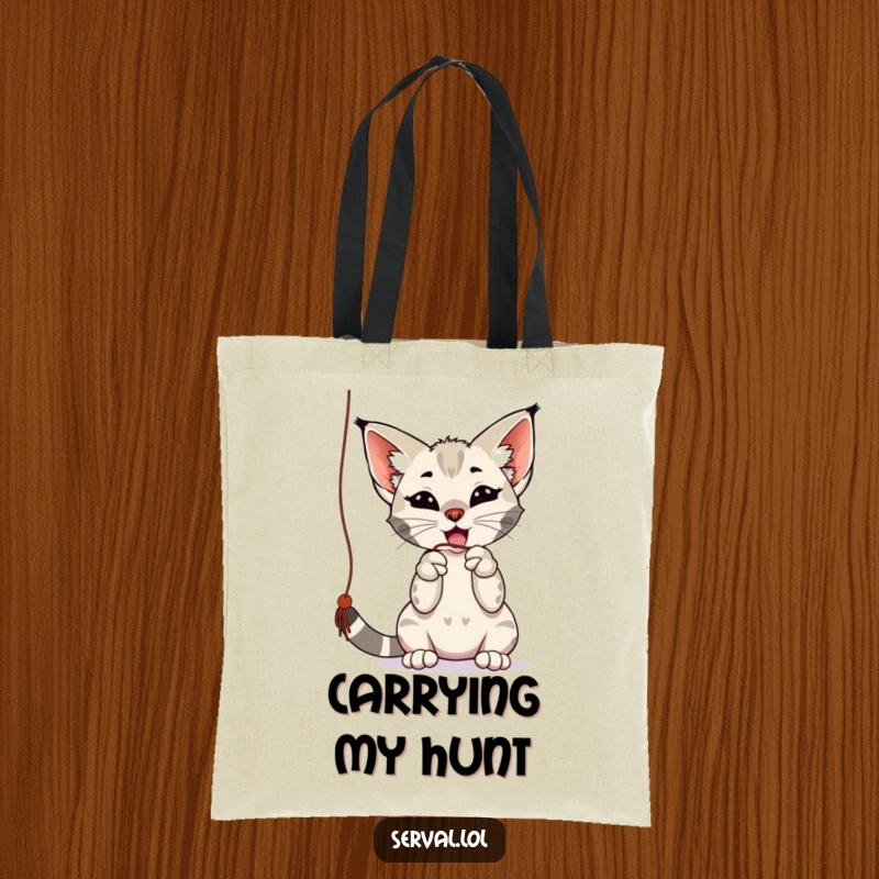 Funny serval tote bag showing a playful serval batting at a dangling string with its paws, perfect for shopping and as a funny gift.